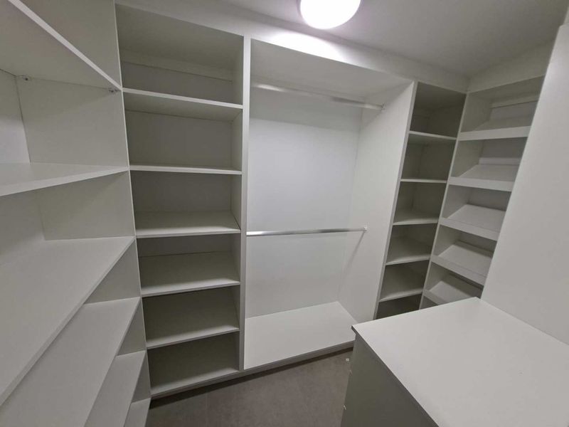 A clean, modern walk-in closet featuring extensive white built-in shelving, hanging rails, and organized storage compartments.