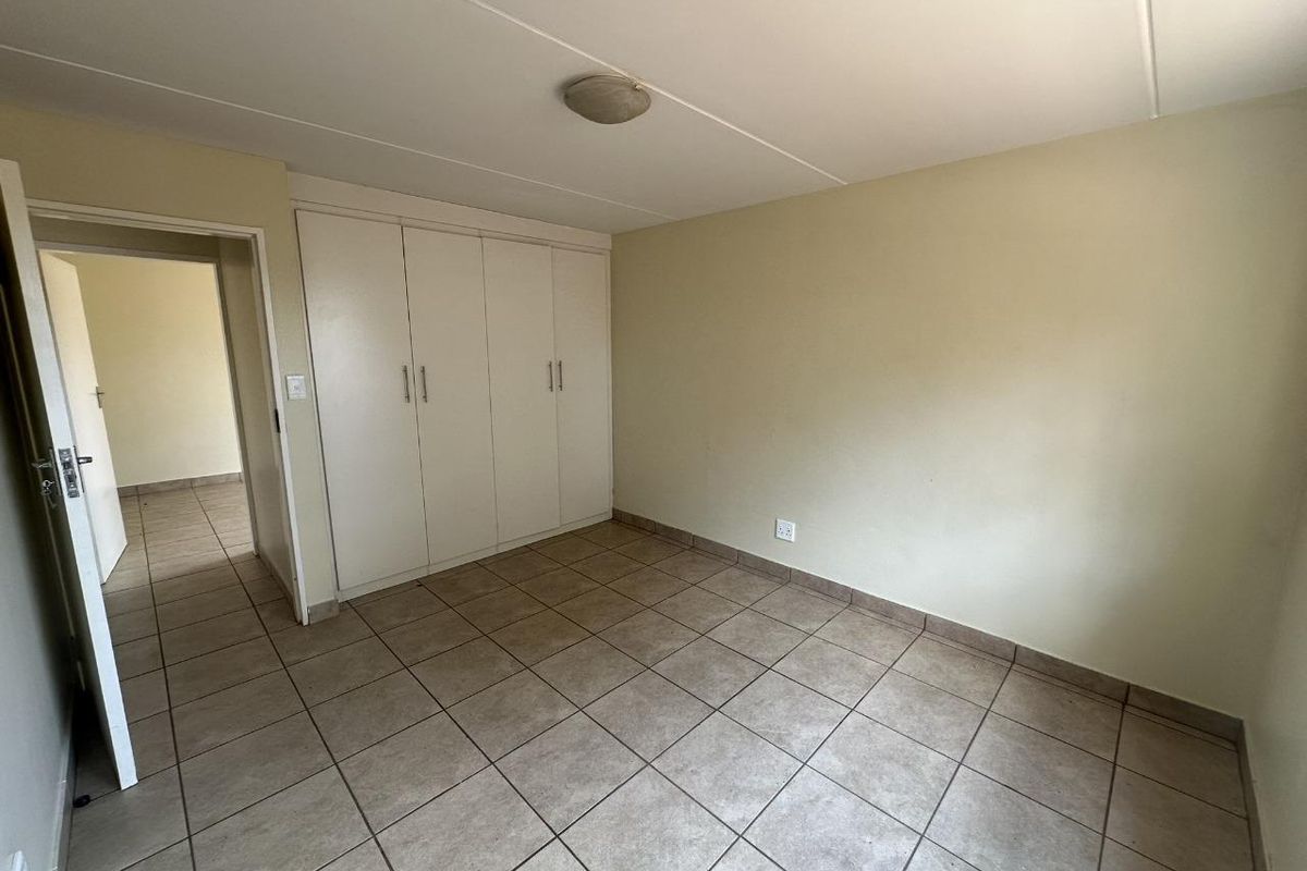 A vacant bedroom featuring built-in cupboards, tiled flooring, and a neutral color palette, offering a blank canvas for personalization.