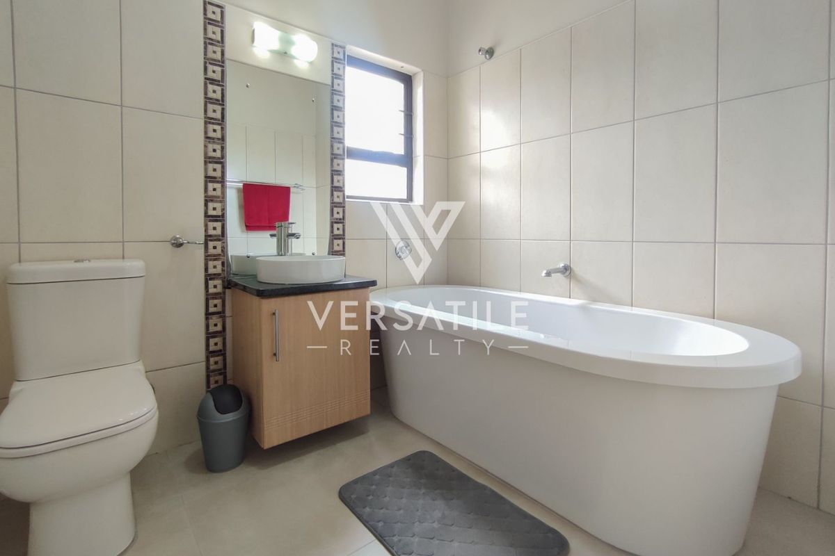 A functional bathroom featuring a freestanding bathtub, a vanity with a vessel sink, and a toilet, finished with neutral wall and floor tiles.