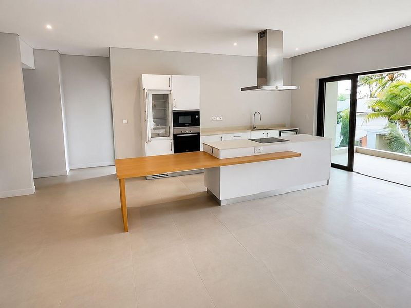 Modern open-plan kitchen featuring a central island with breakfast bar, integrated appliances, and seamless access to a private balcony through large sliding doors.