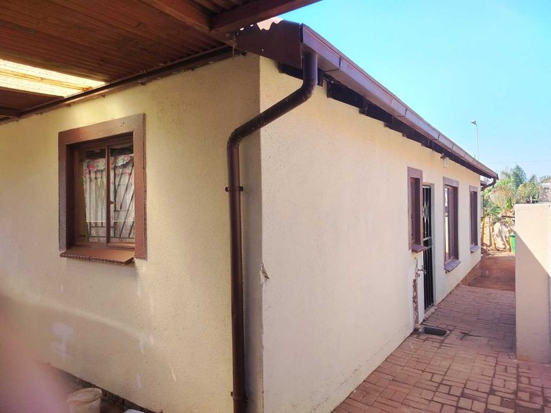 Rear exterior view of the property featuring a paved walkway, security gates, and functional rainwater drainage system along the side elevation.