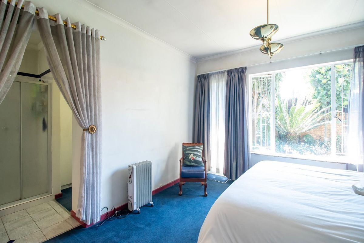 A bedroom featuring an en-suite bathroom, large windows with garden views, and carpeted flooring.
