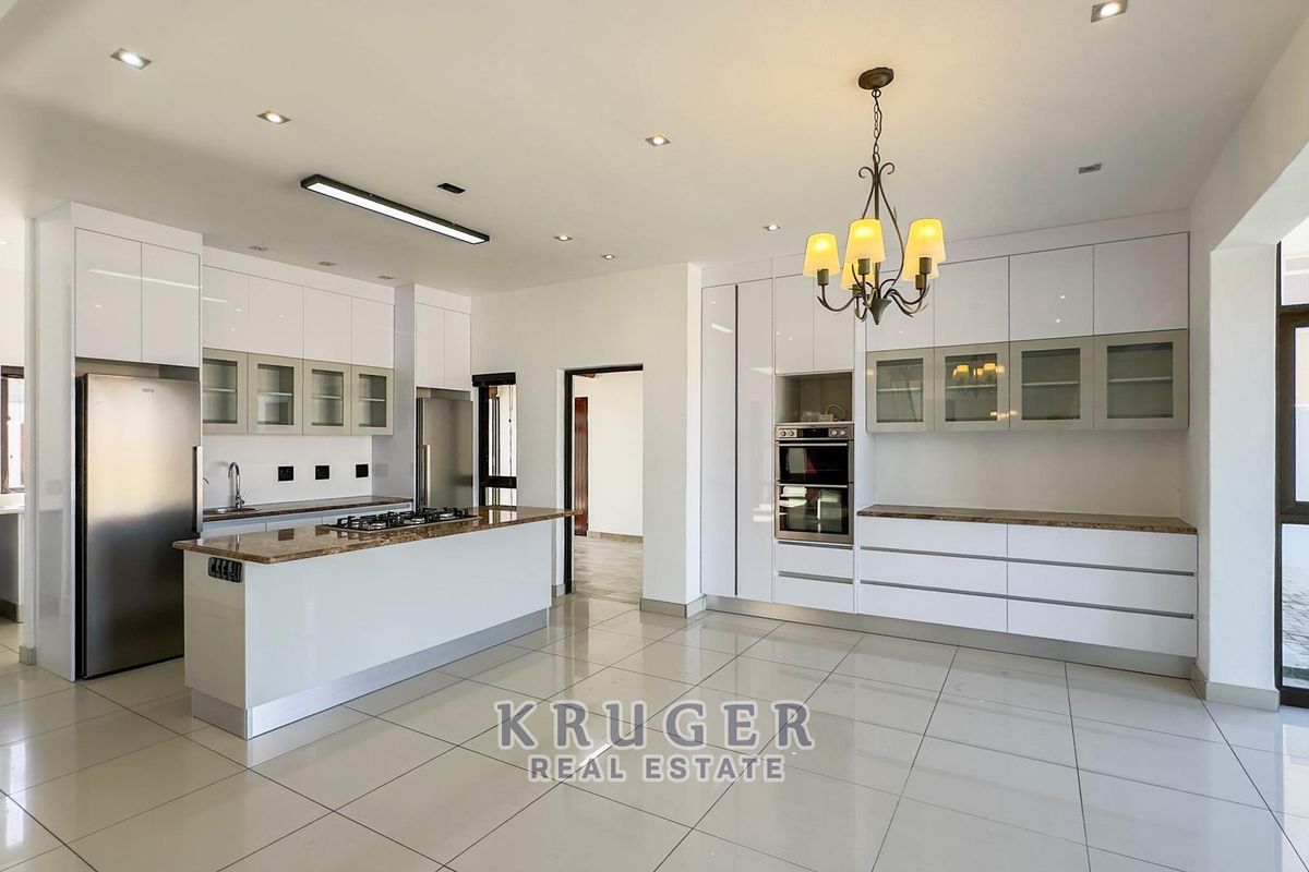 Modern kitchen featuring high-gloss cabinetry, stone countertops, a central island with a built-in gas hob, and integrated wall ovens.