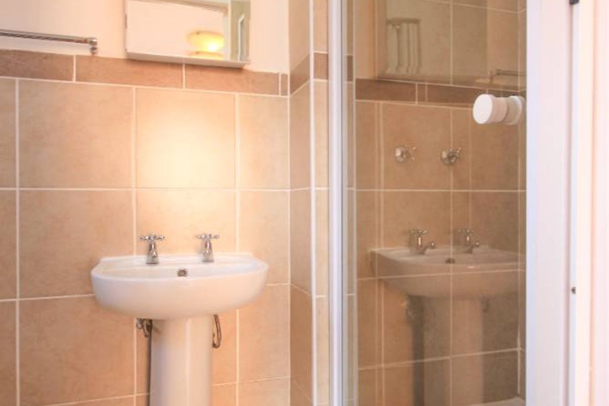 A functional bathroom featuring a pedestal basin, tiled walls and flooring, and a glass-enclosed shower unit.