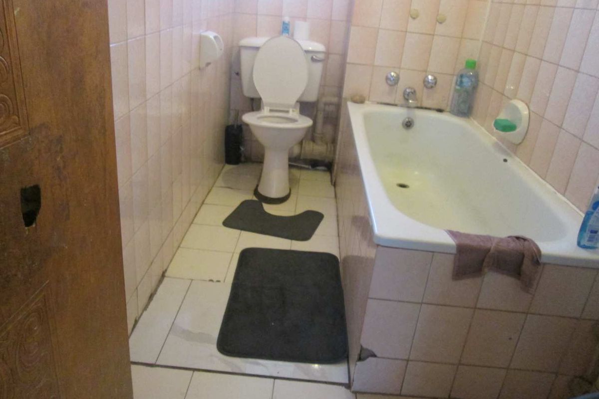A dated bathroom featuring a standard bathtub and toilet with original ceramic wall and floor tiling.