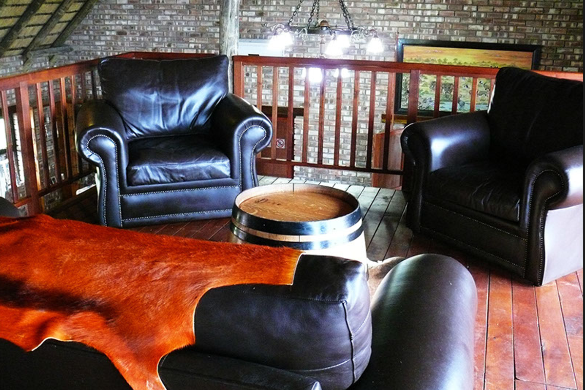 A rustic mezzanine living area featuring exposed brick walls, timber flooring, and a wooden balustrade overlooking the lower level.