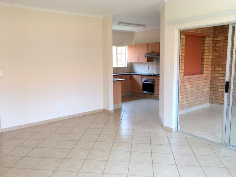 Open-plan living area featuring tiled floors, a functional kitchen with built-in appliances, and a sliding door leading to an enclosed brick-walled patio.