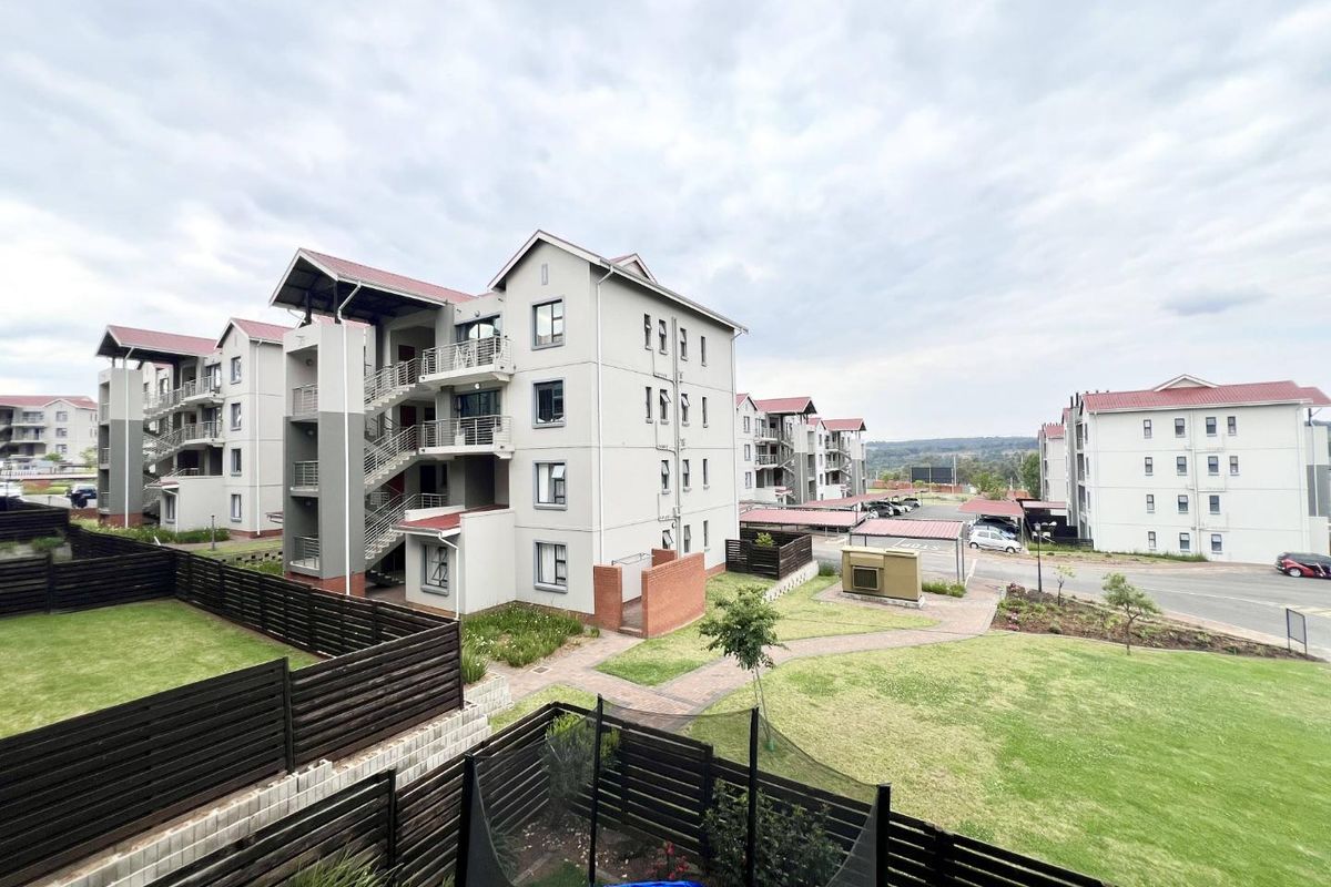 An elevated view of the apartment complex grounds, featuring well-maintained communal gardens, paved pathways, and multi-story residential blocks with balconies and staircases.