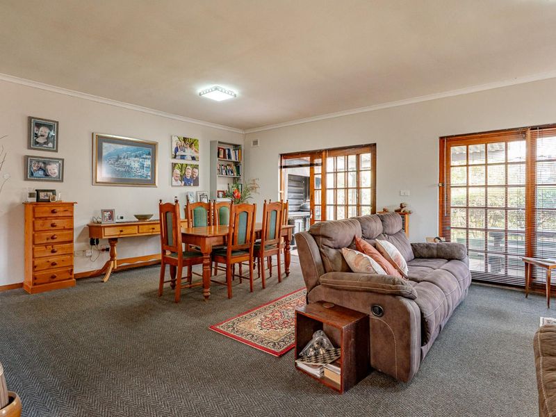 Open-plan living and dining area featuring carpeted flooring, built-in shelving, and timber-framed sliding doors providing access to the outdoor space.