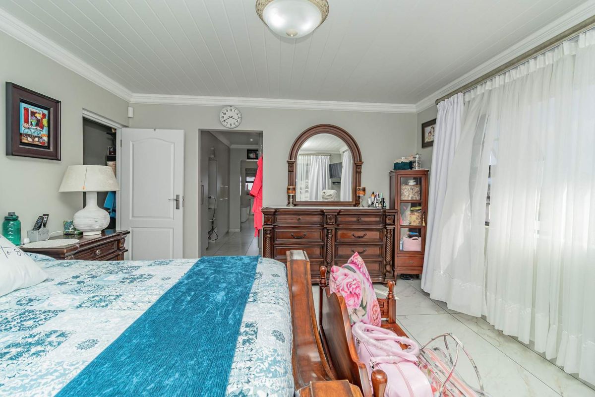 A well-maintained bedroom featuring tiled flooring, crown molding, and a tongue and groove ceiling, with an adjoining en-suite bathroom visible through the doorway.