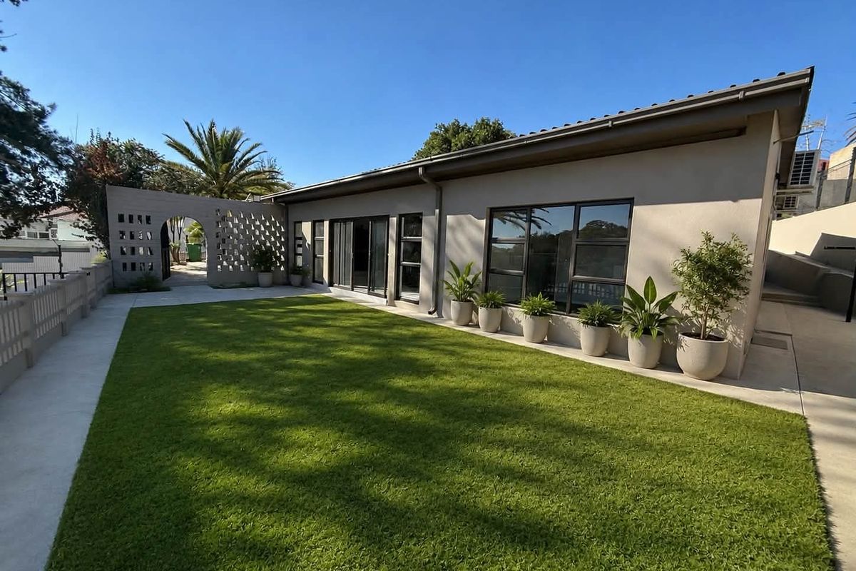 A well-maintained rear exterior featuring a manicured artificial lawn, concrete patio, decorative breeze block wall, and modern aluminium-framed sliding doors.