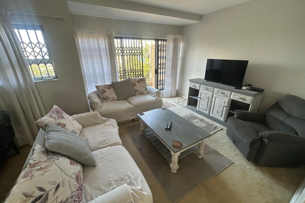 A comfortable living room featuring carpeted flooring, natural light from large windows, and sliding door access to the exterior.