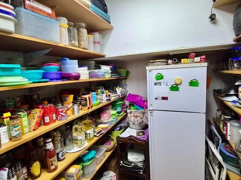 A functional walk-in pantry or scullery area featuring extensive built-in shelving for storage and space for a refrigerator.