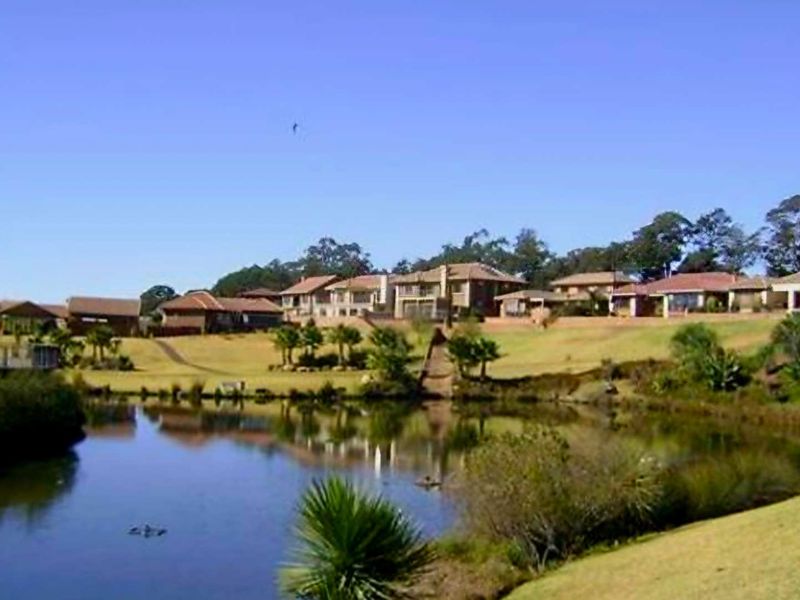 A scenic view of a tranquil lake surrounded by landscaped grounds and residential properties in the distance.