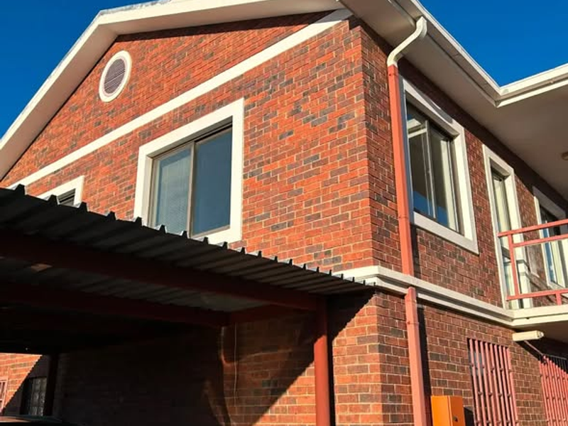 Exterior view of a brick apartment building featuring a carport, balcony, and security bars on ground floor windows.