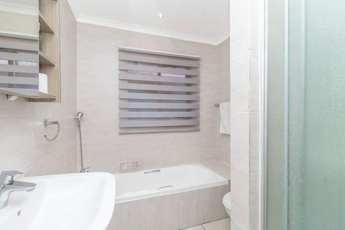 A modern bathroom featuring a built-in bathtub, a separate shower enclosure, a vanity basin, and neutral wall tiling.