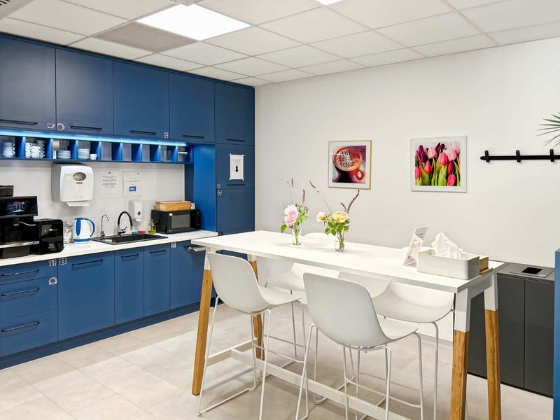 A modern office kitchenette featuring blue cabinetry, integrated sink, and a high-top table, providing a functional break area for staff.