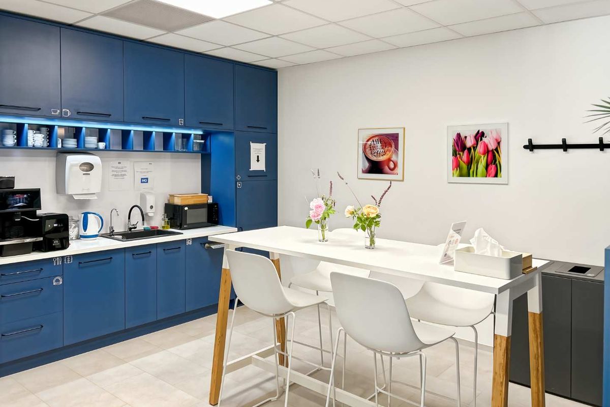 A modern office kitchenette featuring blue cabinetry, integrated sink, and a high-top table, providing a functional break area for staff.