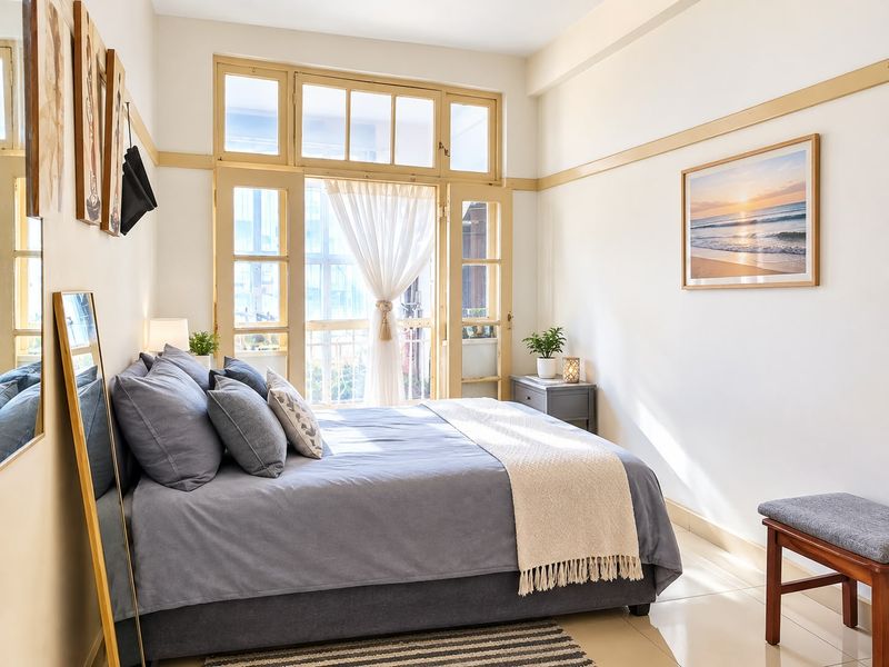 A bright and well-maintained bedroom featuring tiled flooring, a classic picture rail, and large timber-framed glass doors providing natural light and balcony access.