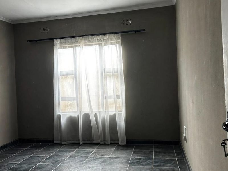 An empty bedroom featuring dark tiled flooring and neutral walls, offering a blank canvas for personalization and interior design updates.