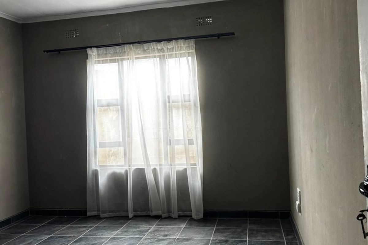 An empty bedroom featuring dark tiled flooring and neutral walls, offering a blank canvas for personalization and interior design updates.