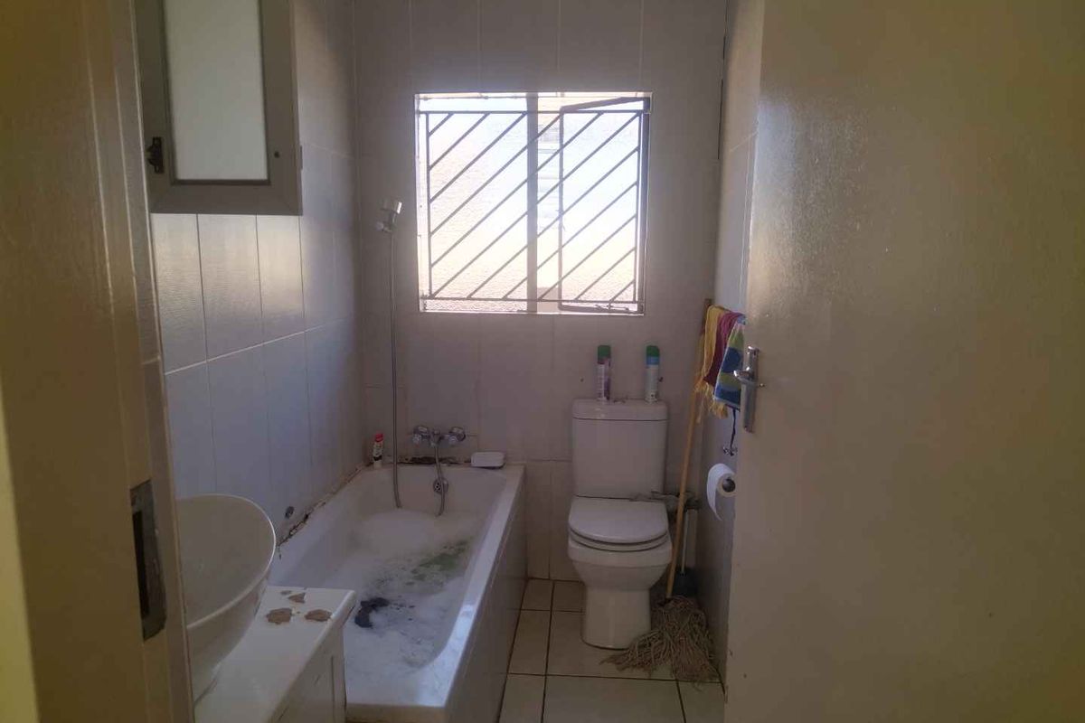 A compact bathroom featuring a built-in bathtub, toilet, and tiled walls. The space requires cosmetic updates to improve its overall condition.