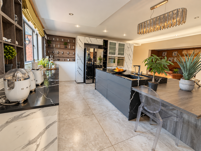 Modern kitchen featuring a large island with marble-look countertops, integrated double ovens, sleek cabinetry, and high-end pendant lighting in an open-plan layout.