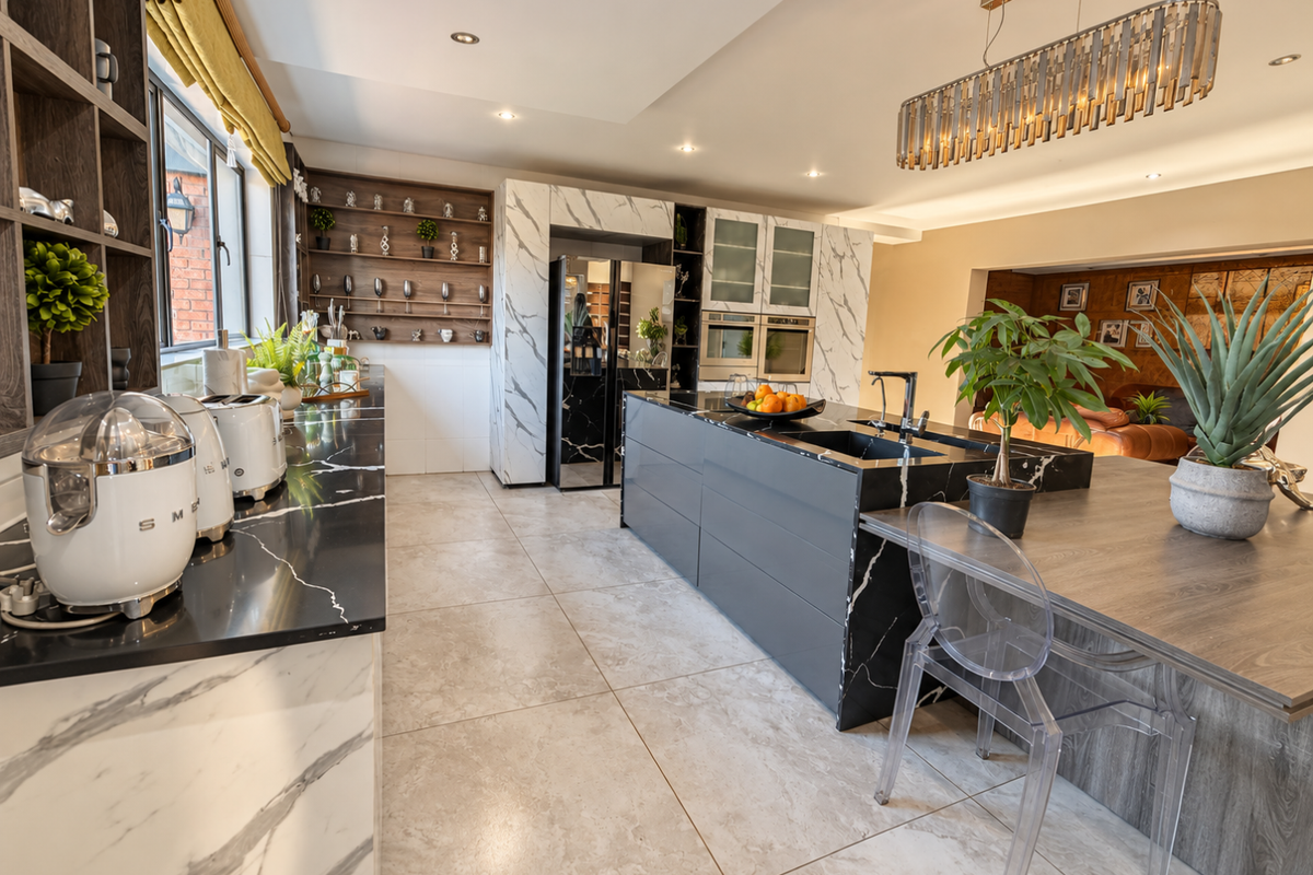 Modern kitchen featuring a large island with marble-look countertops, integrated double ovens, sleek cabinetry, and high-end pendant lighting in an open-plan layout.