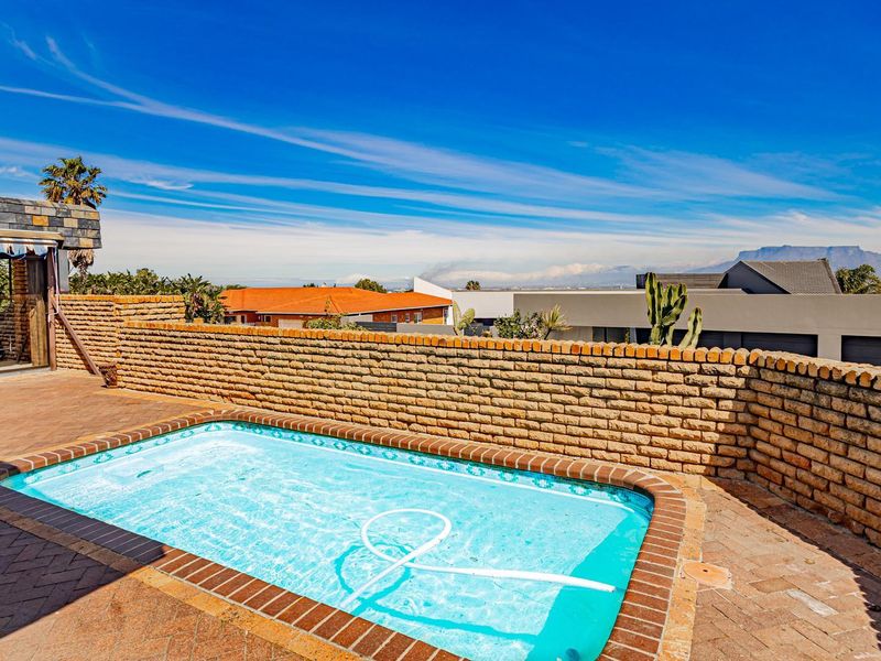 Outdoor pool area featuring a paved patio, brick boundary wall, and a covered patio section with scenic mountain views.