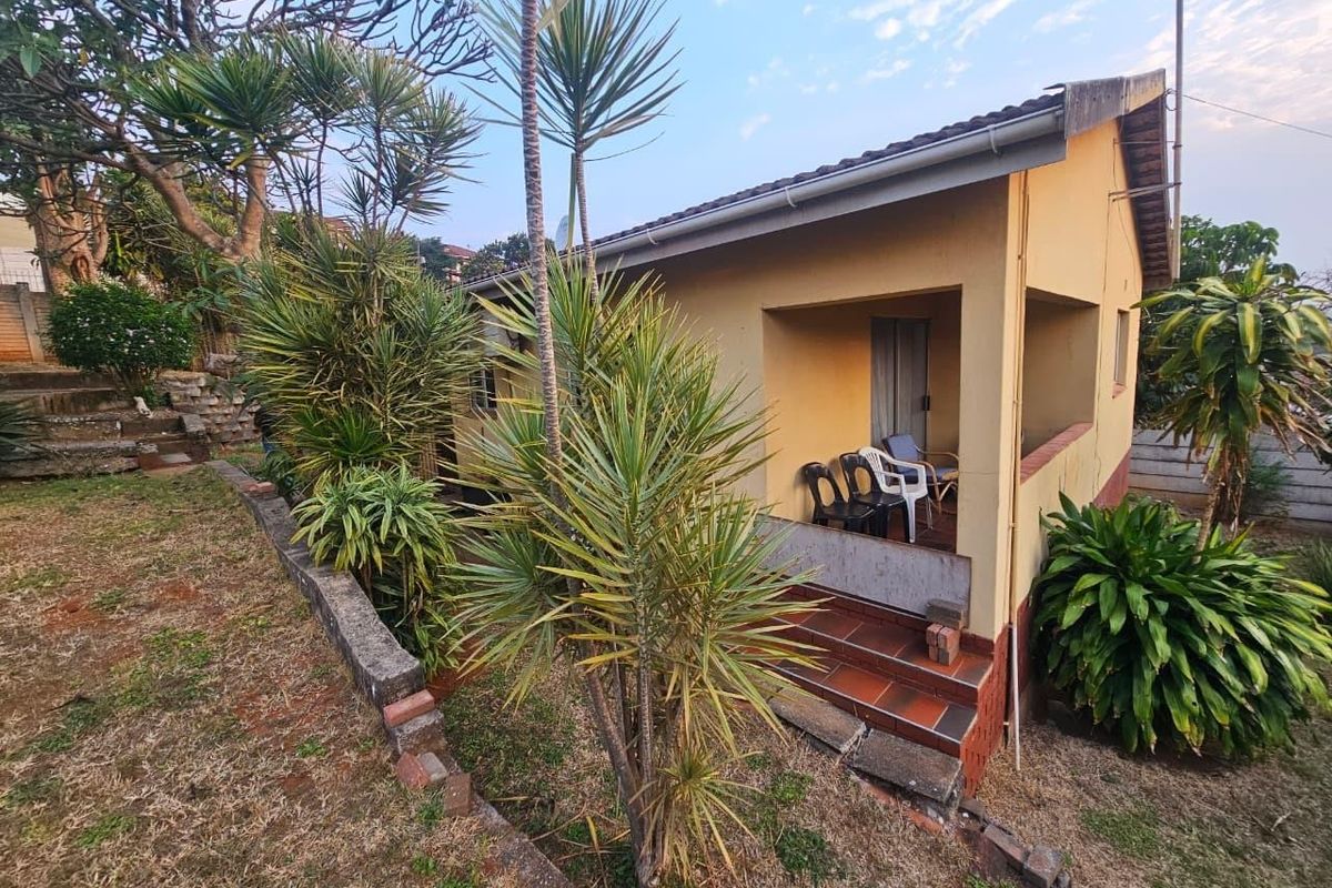 Rear view of the house featuring a covered patio area, tiled roof, and established garden with a brick retaining wall.