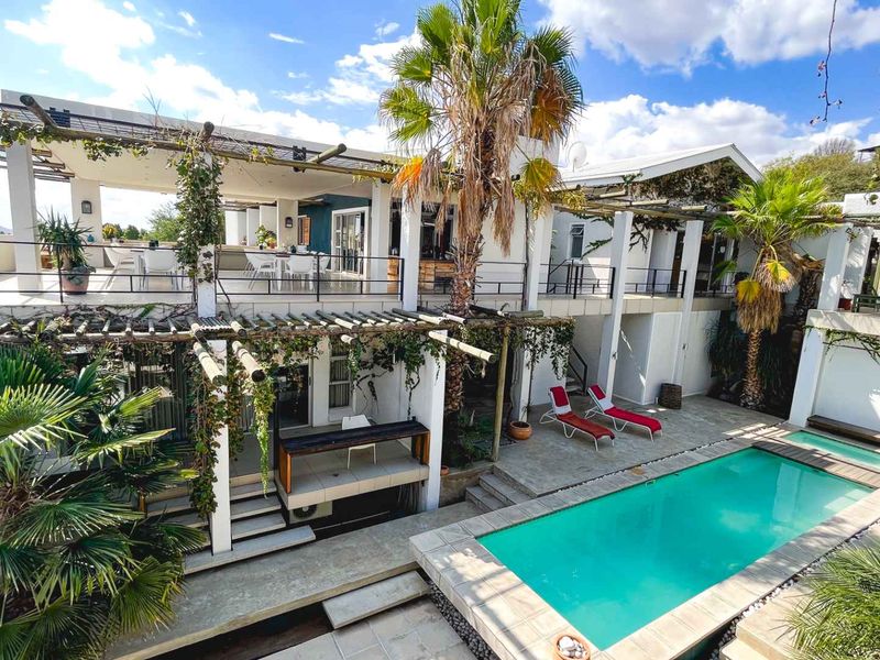 Spacious outdoor entertainment area featuring a swimming pool, multi-level stone patios, and covered pergola structures, ideal for guest house relaxation and leisure.