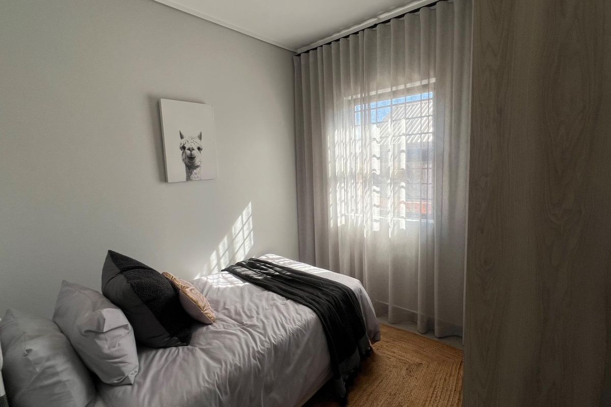 A well-lit bedroom featuring neutral walls, a window with floor-to-ceiling curtains, and a built-in wardrobe.