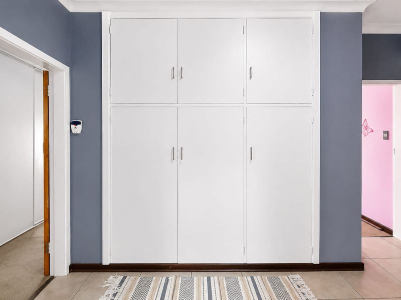 A clean, well-maintained hallway featuring extensive built-in white cabinetry for storage, neutral tiled flooring, and modern grey wall finishes.
