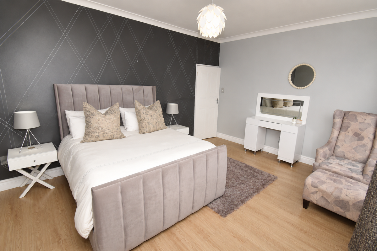 A well-maintained bedroom featuring light wood-look flooring, a decorative accent wall, and a classic door, offering a clean and comfortable living space.