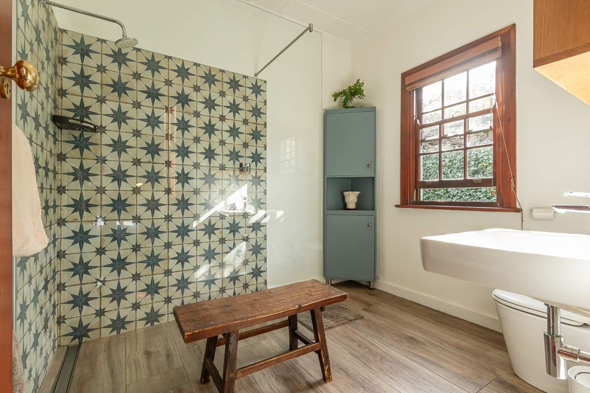 A bright, modern bathroom featuring a walk-in shower with decorative patterned tiles, a wall-mounted basin, and a built-in corner storage cabinet.