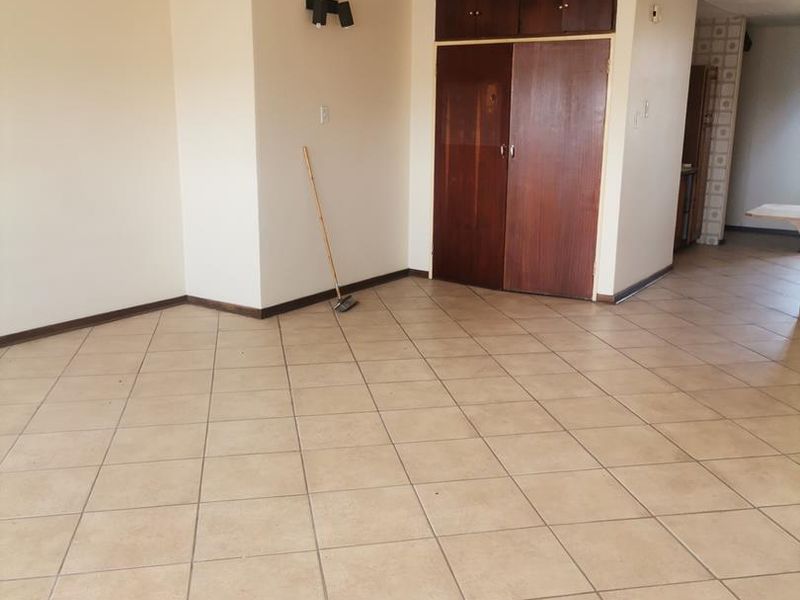 An empty living area featuring ceramic tiled flooring, built-in wooden storage cupboards, and adjustable track lighting.