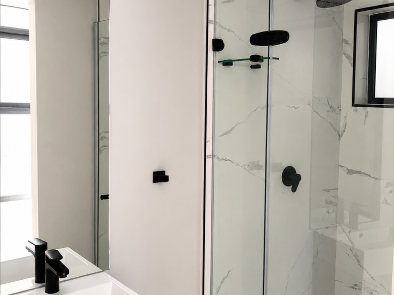 Modern bathroom featuring a sleek vanity with black fixtures, a glass-enclosed shower with marble-look tiling, and contemporary recessed ceiling lighting.