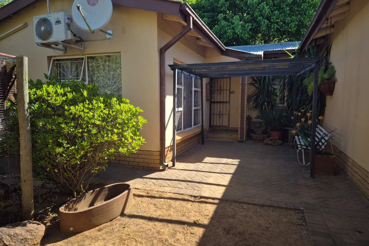 A paved rear courtyard area featuring a metal pergola structure, exterior wall-mounted air conditioning unit, and security gates on windows and doors.