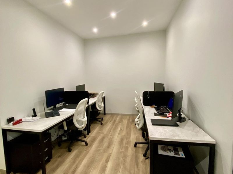 A modern, well-lit office space featuring wood-look laminate flooring and recessed ceiling lighting, configured with dual workstations.
