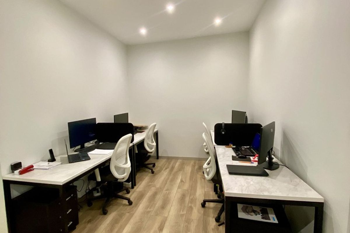 A modern, well-lit office space featuring wood-look laminate flooring and recessed ceiling lighting, configured with dual workstations.