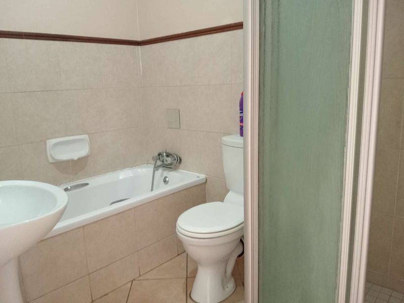 A functional bathroom featuring a bathtub, pedestal basin, toilet, and a separate shower enclosure with neutral ceramic tiling throughout.