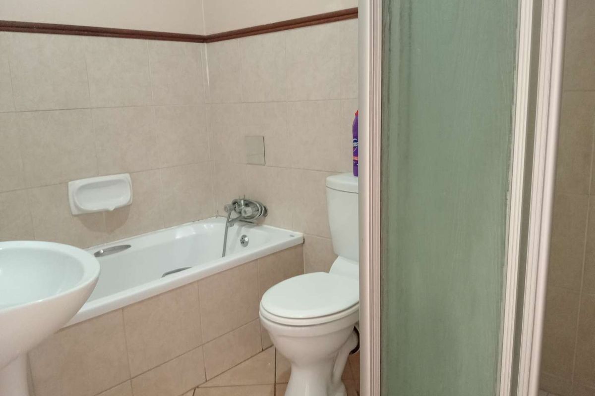 A functional bathroom featuring a bathtub, pedestal basin, toilet, and a separate shower enclosure with neutral ceramic tiling throughout.