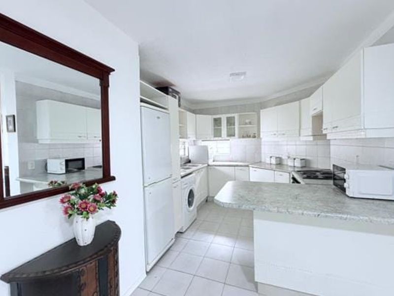 A functional kitchen featuring white cabinetry, laminate countertops, tiled flooring, and a breakfast bar, offering a clean and practical layout for daily use.