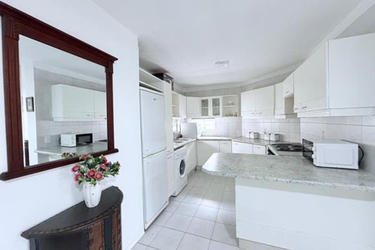 A functional kitchen featuring white cabinetry, laminate countertops, tiled flooring, and a breakfast bar, offering a clean and practical layout for daily use.