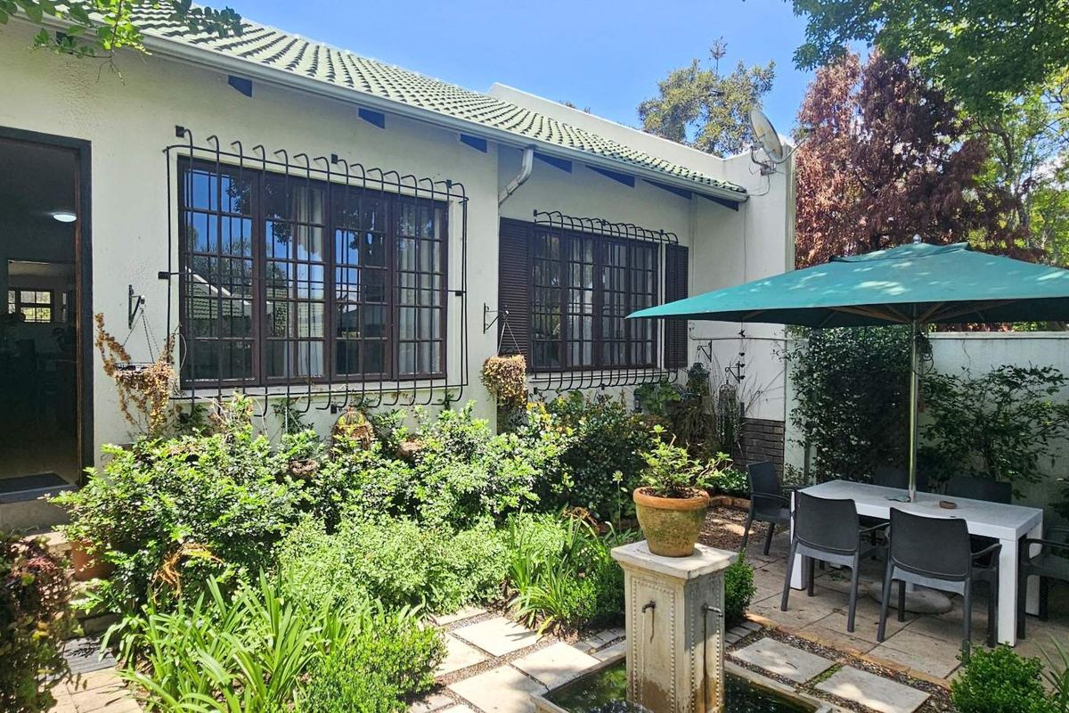 A private rear garden featuring a paved patio area, built-in outdoor fireplace, and established landscaping adjacent to the home's rear facade.