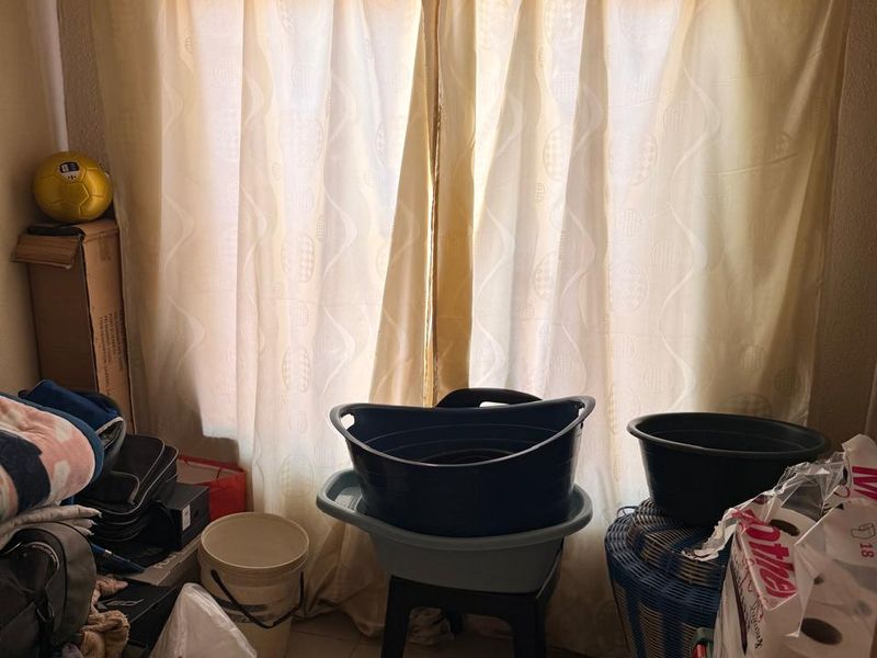 A small room featuring tiled flooring and a window with curtains, currently used for storage.