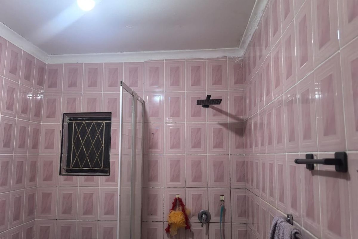 A bathroom featuring pink wall tiles, a shower enclosure, and modern black fixtures. The space is ready for a cosmetic update.