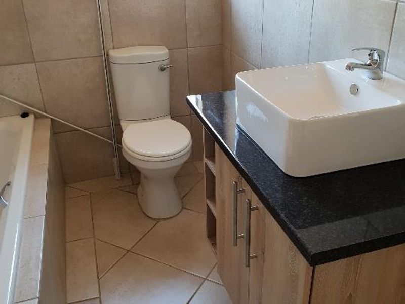 A functional bathroom featuring a vessel sink on a granite vanity, a toilet, and a bathtub with neutral ceramic tiling throughout.