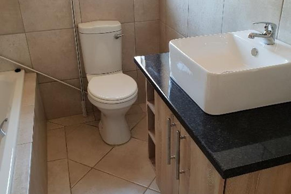 A functional bathroom featuring a vessel sink on a granite vanity, a toilet, and a bathtub with neutral ceramic tiling throughout.