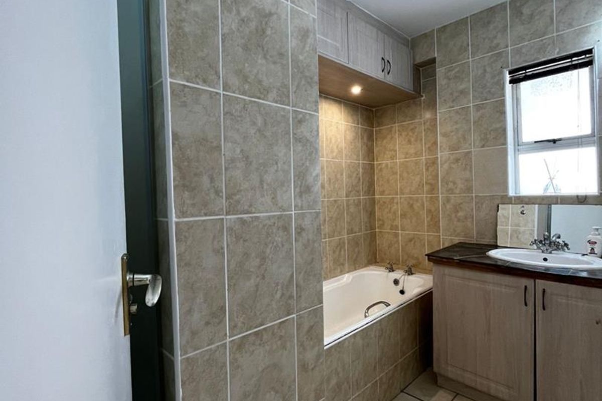 A functional bathroom featuring a built-in bathtub with tiled surround, vanity cabinet with integrated basin, and overhead storage cabinetry.